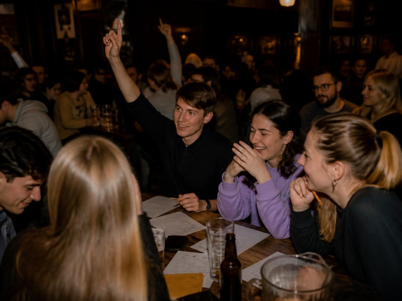 Soirée quiz dans un bar : des étudiants autour d'une table en bois avec des feuilles de réponses